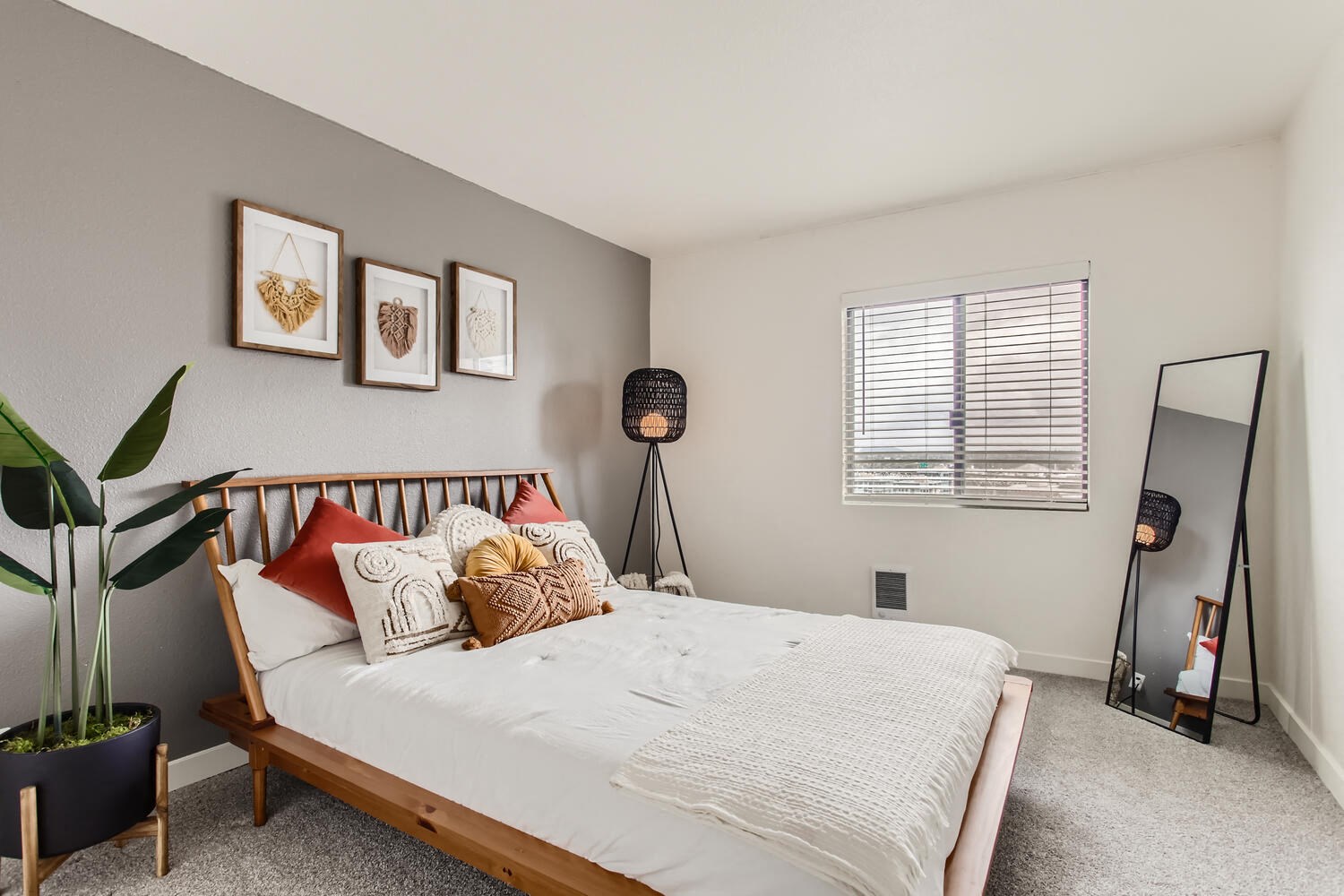 Downtown Portland, OR, Modern Apartments - Linc 301 - Bedroom with Carpet Flooring, Large, Wooden Bed, Standing Lamp, Full-Body Mirror, Decorative Potted Plant, and Window.